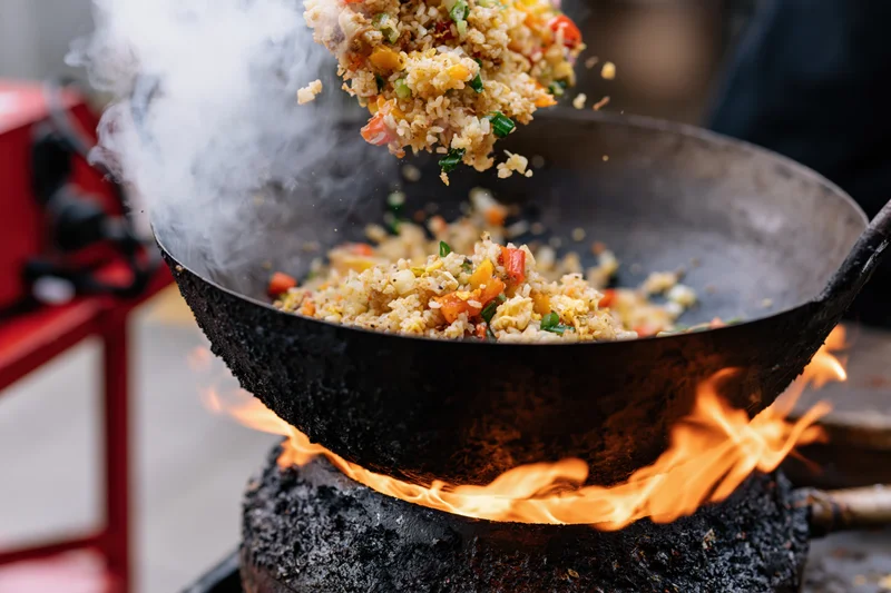 Stir-fried rice and vegetables being tossed in a wok over open flames