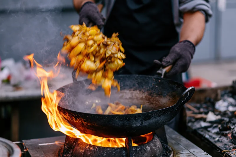 Street cook tossing vegetables in a wok over an open flame outdoors
