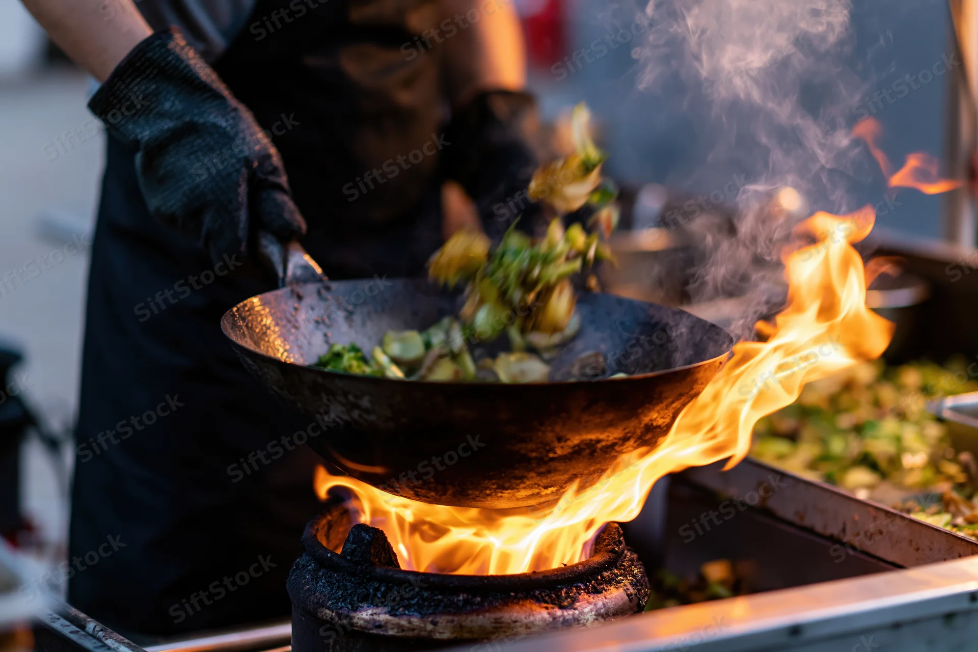 Chef tossing vegetables in a wok over an open flame at a street food stall