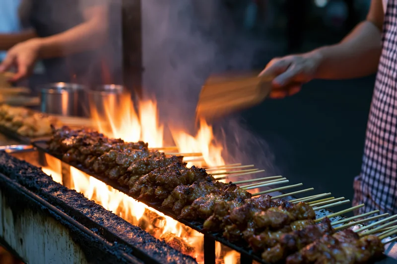 Rows of meat satay skewers grilling over open flame at night market