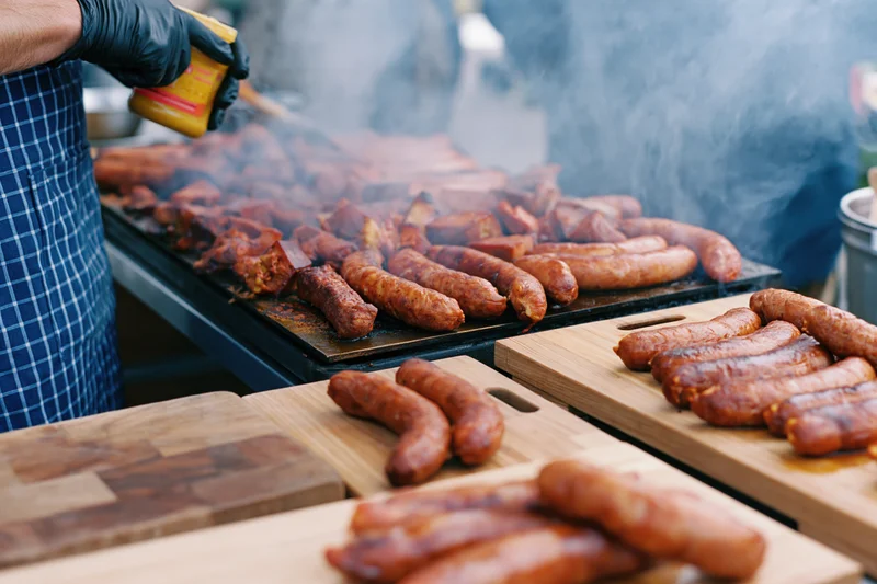 Street food vendor grilling sausages on a barbecue grill outdoors