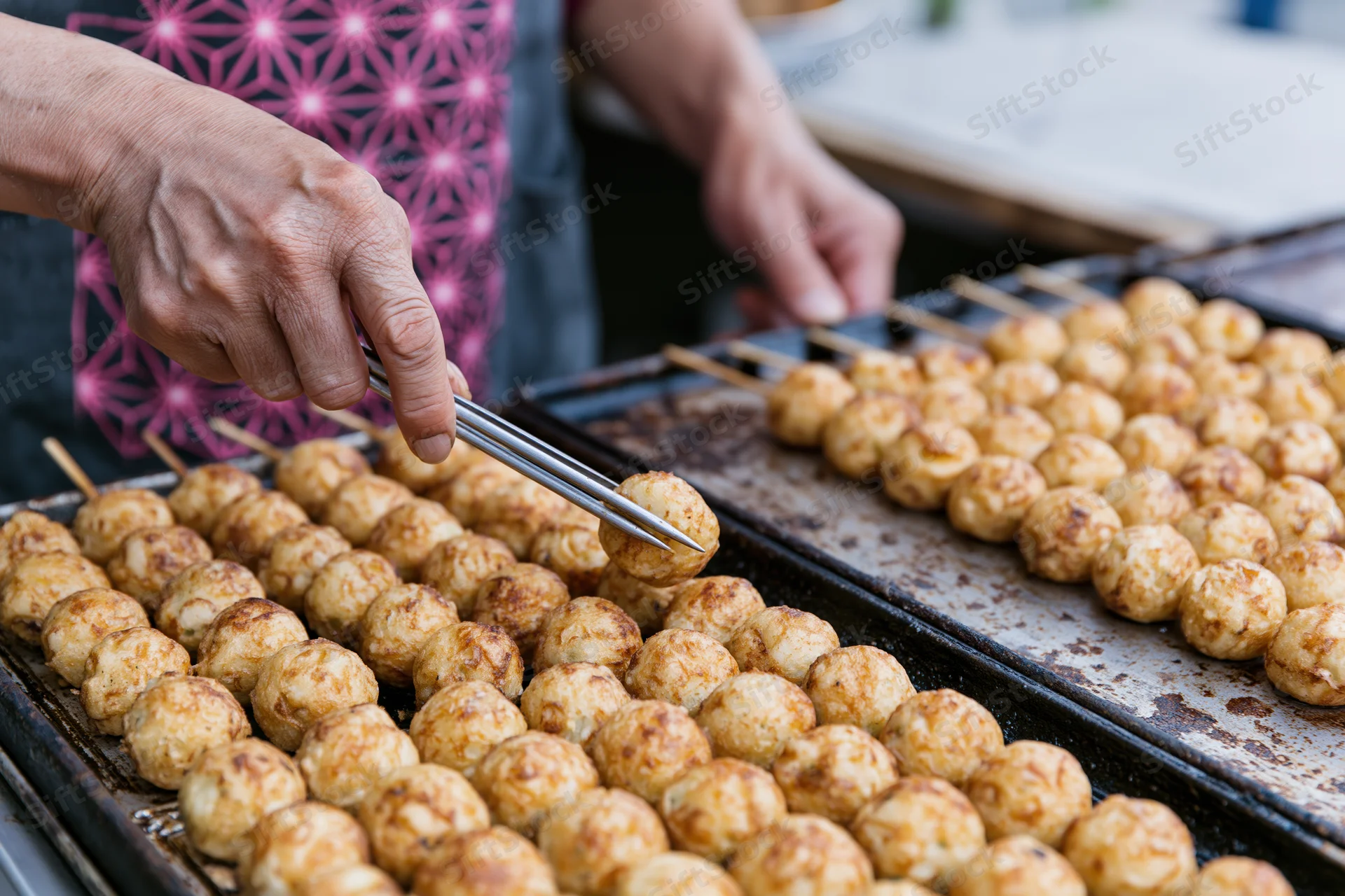 Vendor hands flipping rows of takoyaki on a grill at a street food market