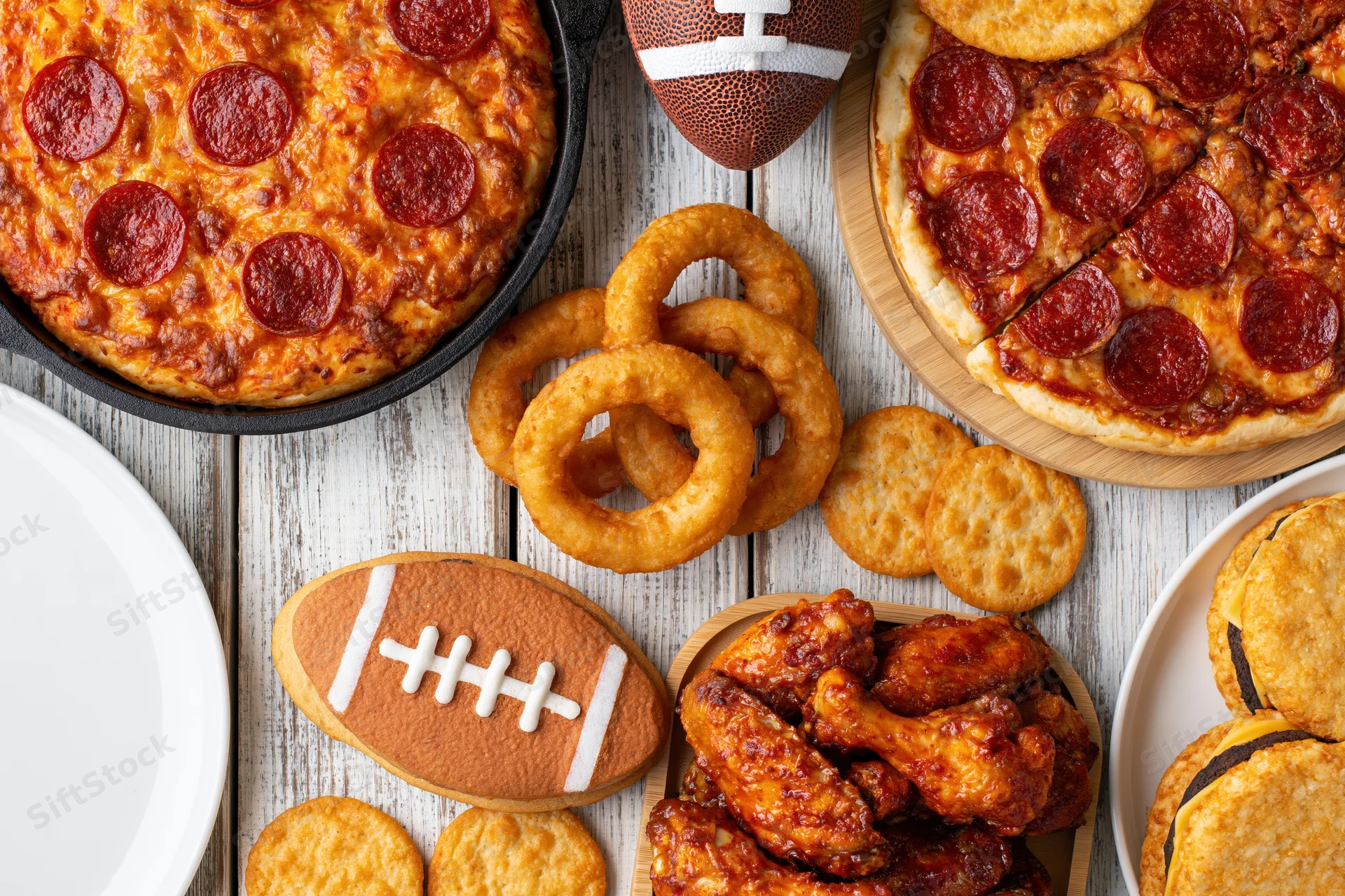 Pepperoni pizza and game-themed snacks arranged on a weathered white wooden table for a football party