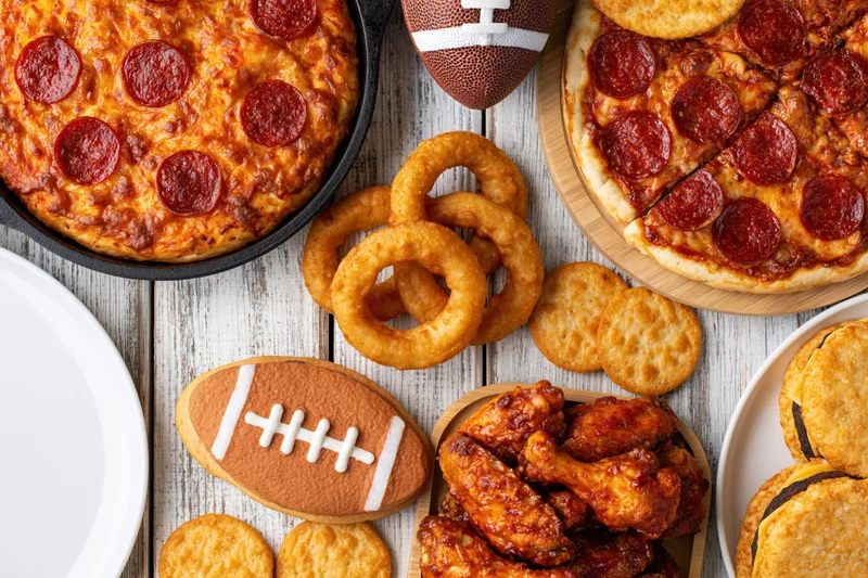 Pepperoni pizza and game-themed snacks arranged on a weathered white wooden table for a football party
