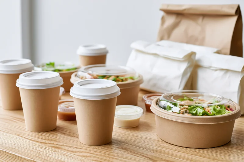 Takeout food containers and coffee cups arranged on a light wooden table