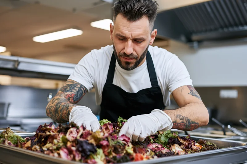 Tattooed male chef sorting fresh salad ingredients in a commercial kitchen