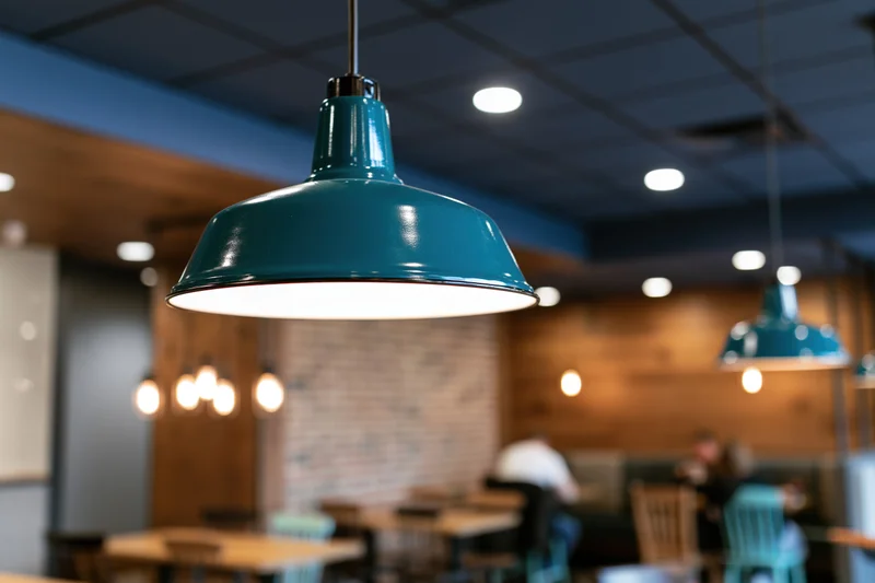 Teal enamel pendant lamp hanging from dark blue ceiling in restaurant interior