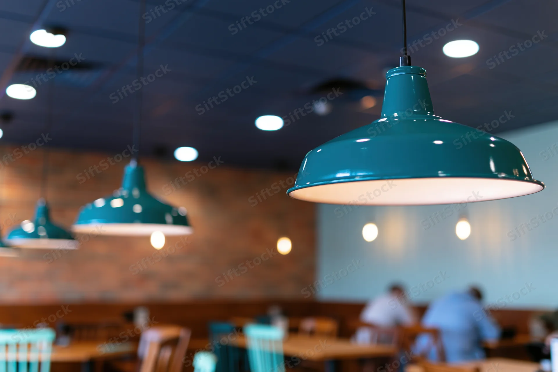 Teal enamel pendant lamps hanging from dark blue ceiling in restaurant dining area