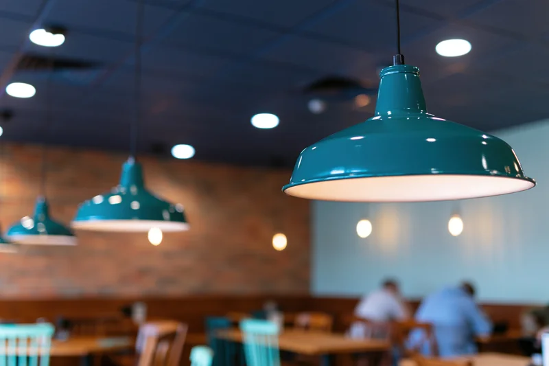Teal enamel pendant lamps hanging from dark blue ceiling in restaurant dining area