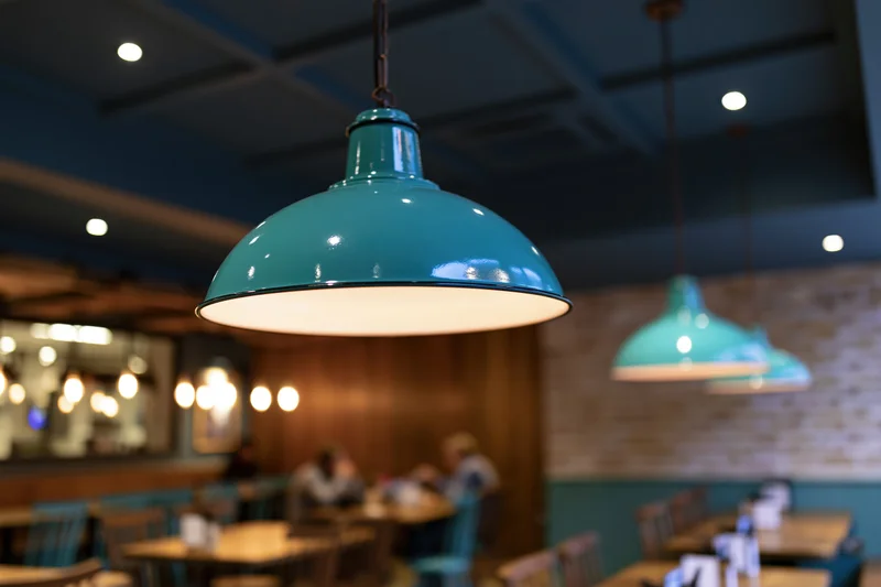 Teal enamel pendant lamps hanging from dark blue ceiling in restaurant interior
