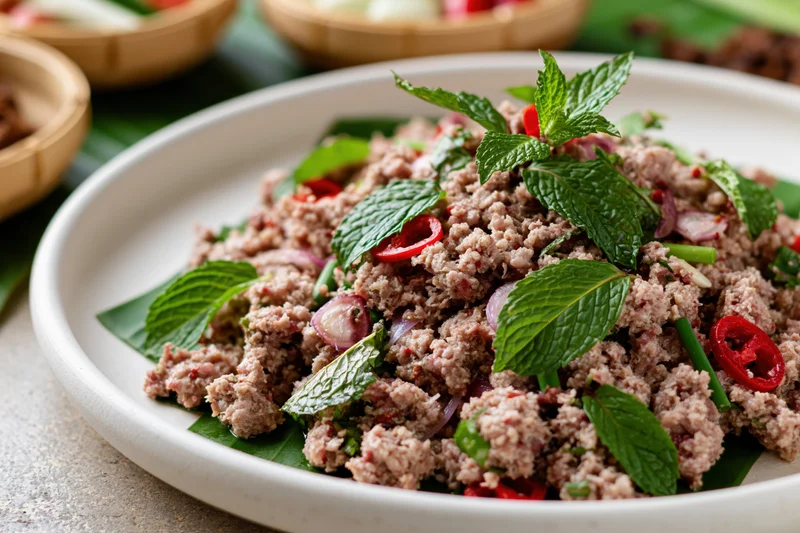 Thai larb moo minced pork salad garnished with mint and chili on a white plate