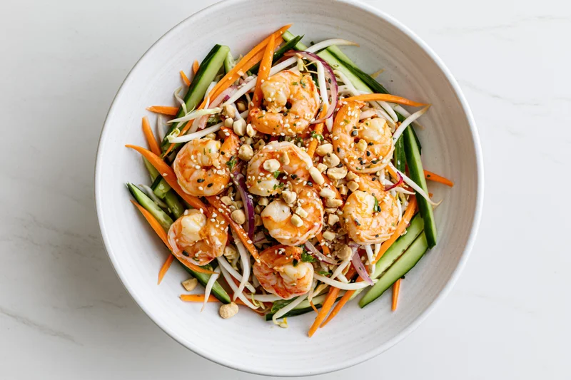Thai shrimp salad with julienned carrots cucumber and bean sprouts in a white bowl on marble surface