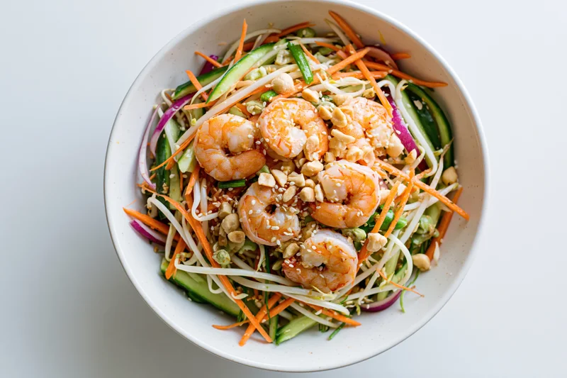 Thai shrimp salad with julienned carrots cucumber and bean sprouts in a white bowl, overhead view
