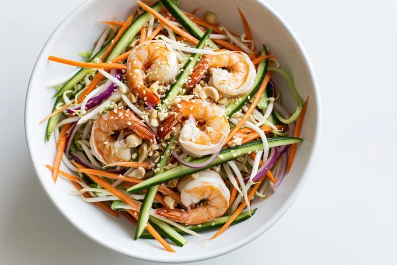 Thai shrimp salad with julienned carrots cucumber and bean sprouts in a white bowl
