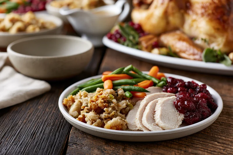 Sliced turkey with stuffing, cranberry sauce, and vegetables on a plate set on a rustic wooden table during thanksgiving dinner