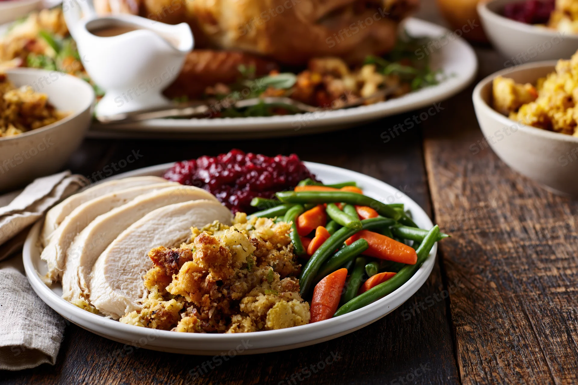 Sliced turkey with stuffing, cranberry sauce, and green beans on a plate at a rustic wooden table during thanksgiving dinner