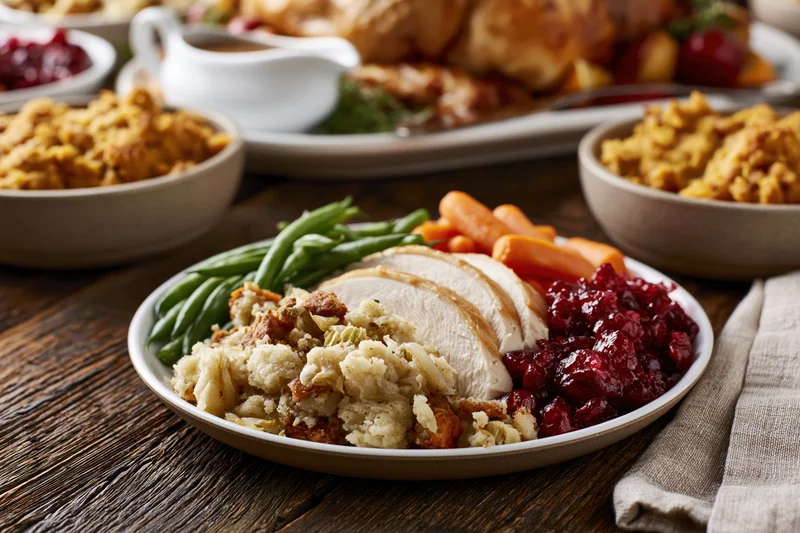 Sliced turkey with stuffing, cranberry sauce, green beans and carrots on a plate at a Thanksgiving dinner table