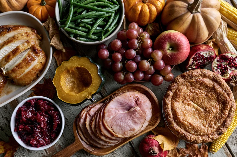 Thanksgiving feast spread on a rustic wooden table with turkey, ham, pie, and autumn produce
