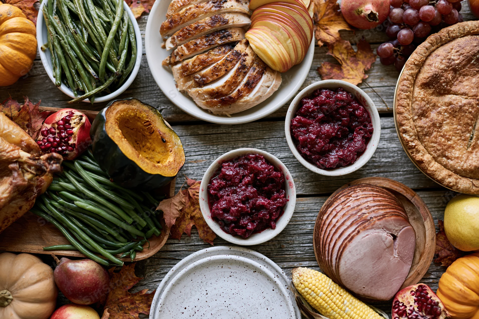 Thanksgiving feast spread on a rustic wooden table with turkey, cranberry sauce, pumpkin, corn, and autumn decorations
