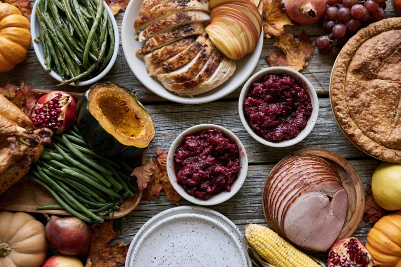 Thanksgiving feast spread on a rustic wooden table with turkey, cranberry sauce, pumpkin, corn, and autumn decorations