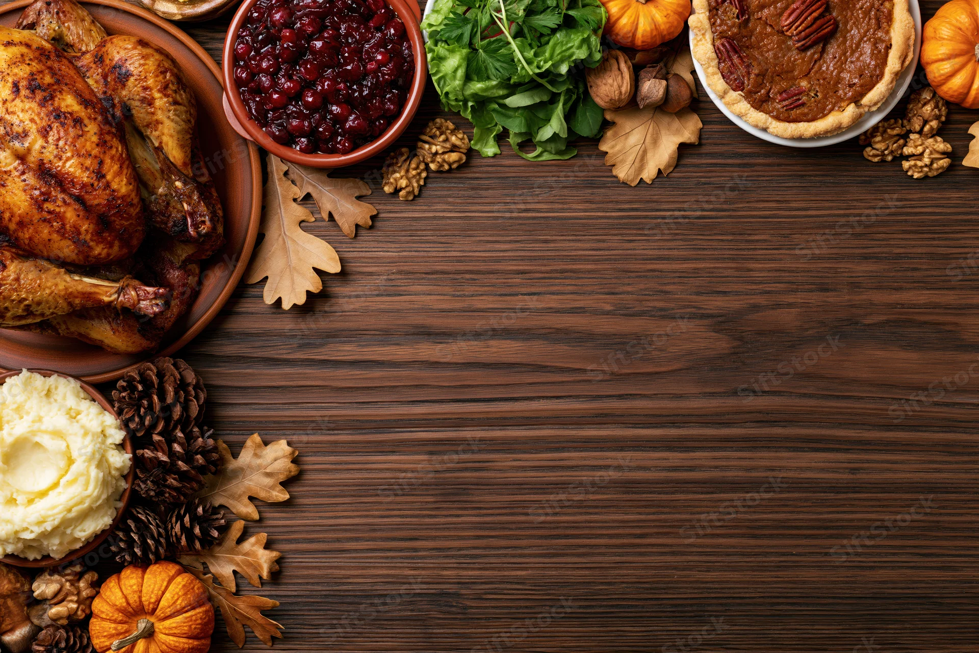 Thanksgiving feast spread with turkey, cranberry sauce, pecan pie and autumn decor arranged along the top edge of a wooden table