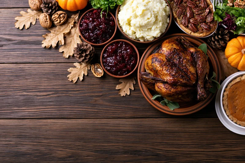 Thanksgiving feast spread with roasted turkey, cranberry sauce, mashed potatoes, pies and autumn decor on wooden table