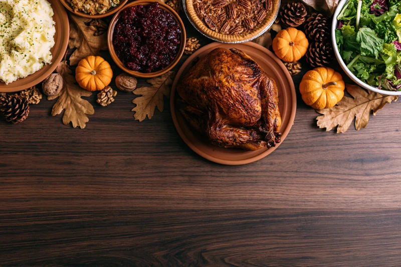 Roasted turkey and Thanksgiving side dishes arranged on a wooden table with autumn decorations along the right side
