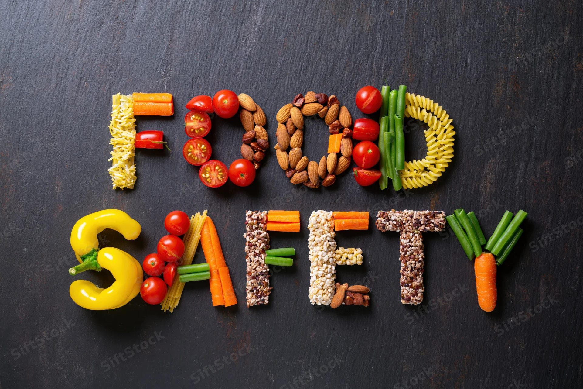 Food safety spelled with vegetables and fruits arranged on dark slate surface