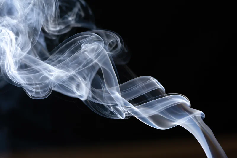 Thin white smoke tendrils curling and rising against a black background