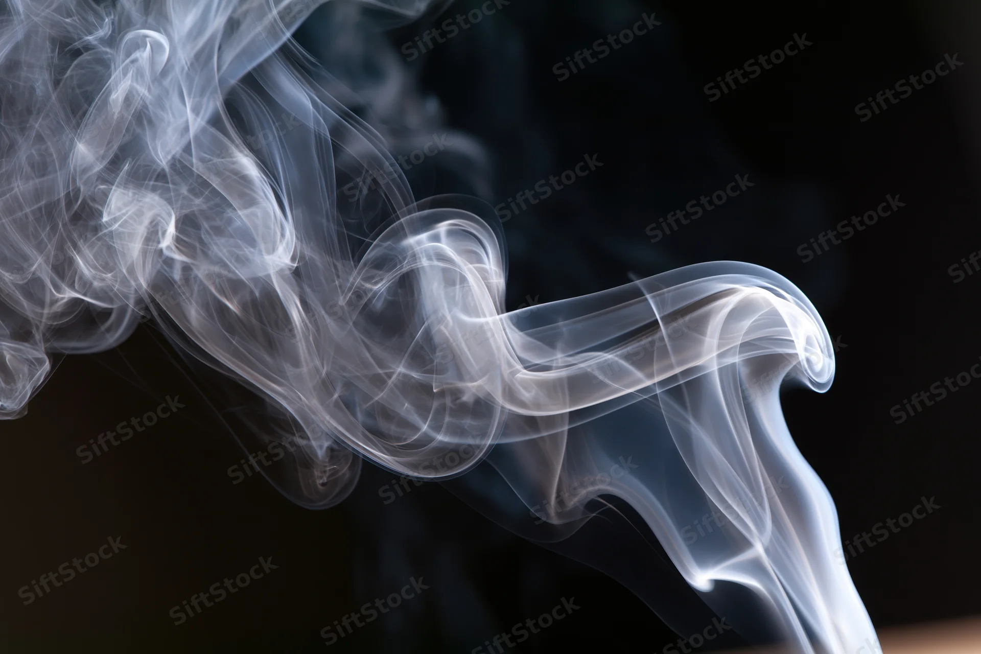 Thin white smoke tendrils curling and rising against a dark background