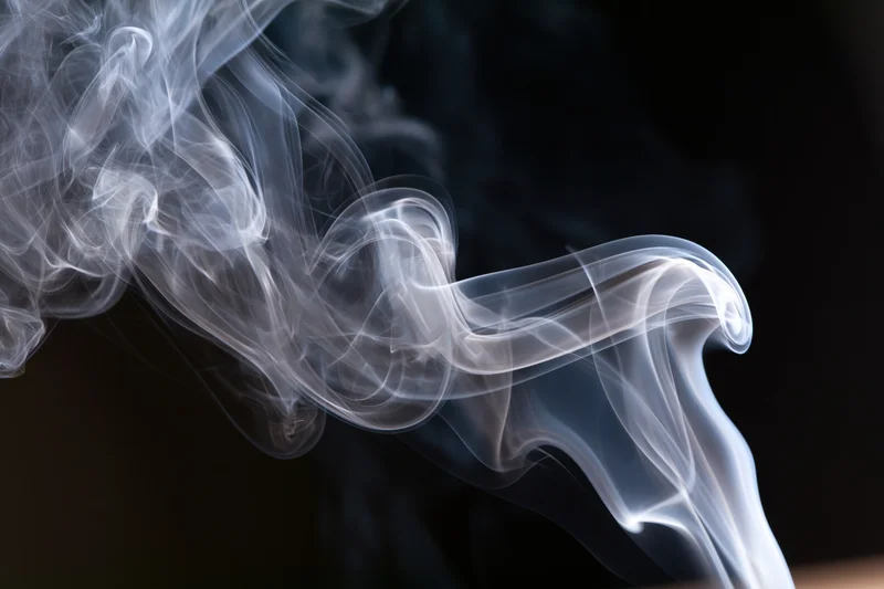 Thin white smoke tendrils curling and rising against a dark background