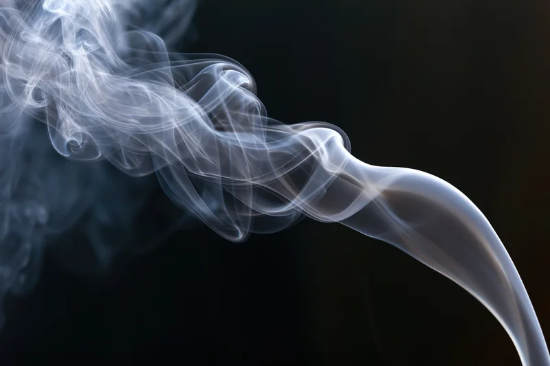 Thin white smoke tendrils curling and rising against a dark background