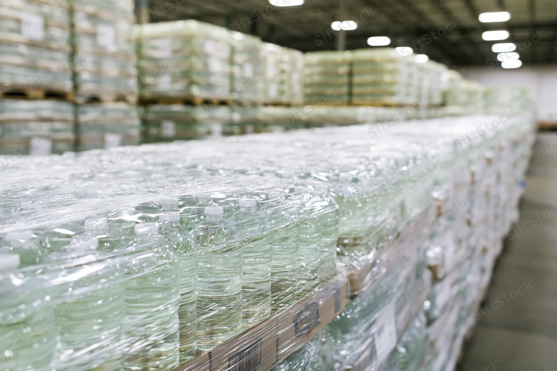 Rows of shrink-wrapped plastic water bottles stacked on pallets in a warehouse
