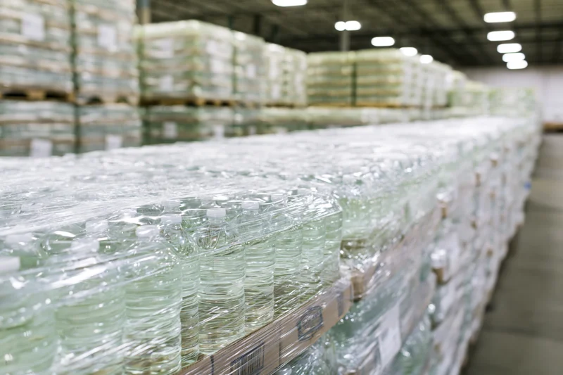 Rows of shrink-wrapped plastic water bottles stacked on pallets in a warehouse