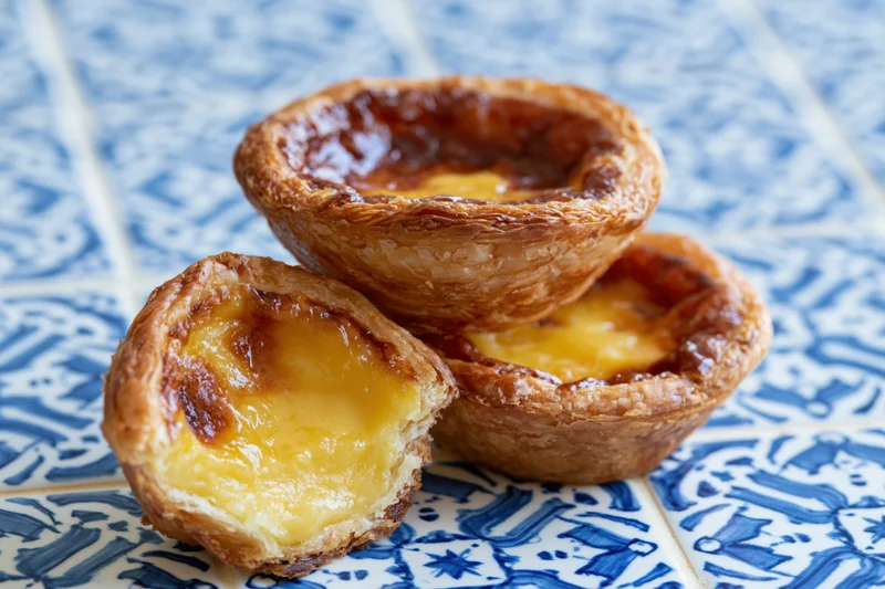 Three pastel de nata egg tarts stacked on a blue patterned tile surface