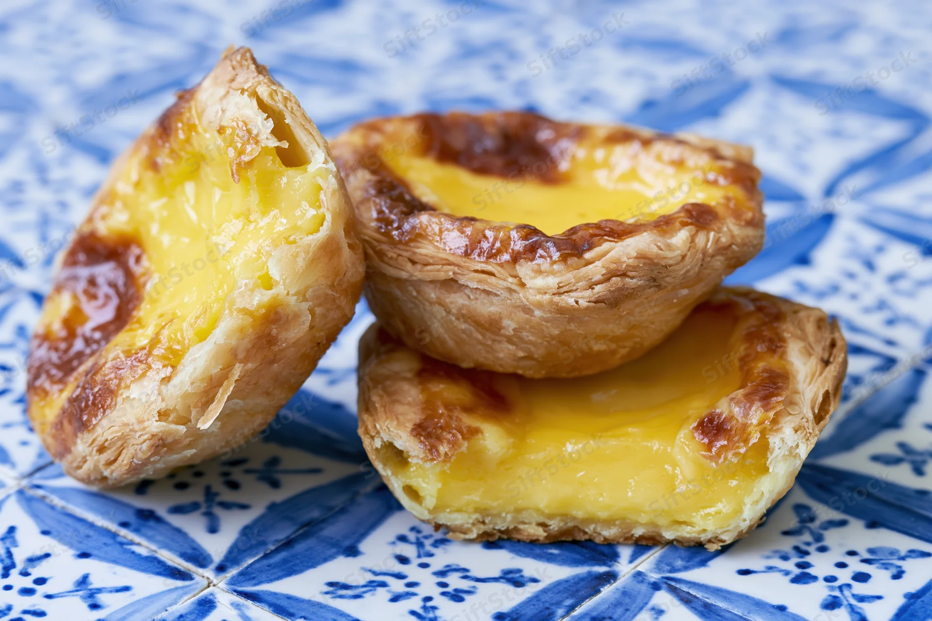 Three pastel de nata egg tarts stacked on a blue and white patterned tile surface