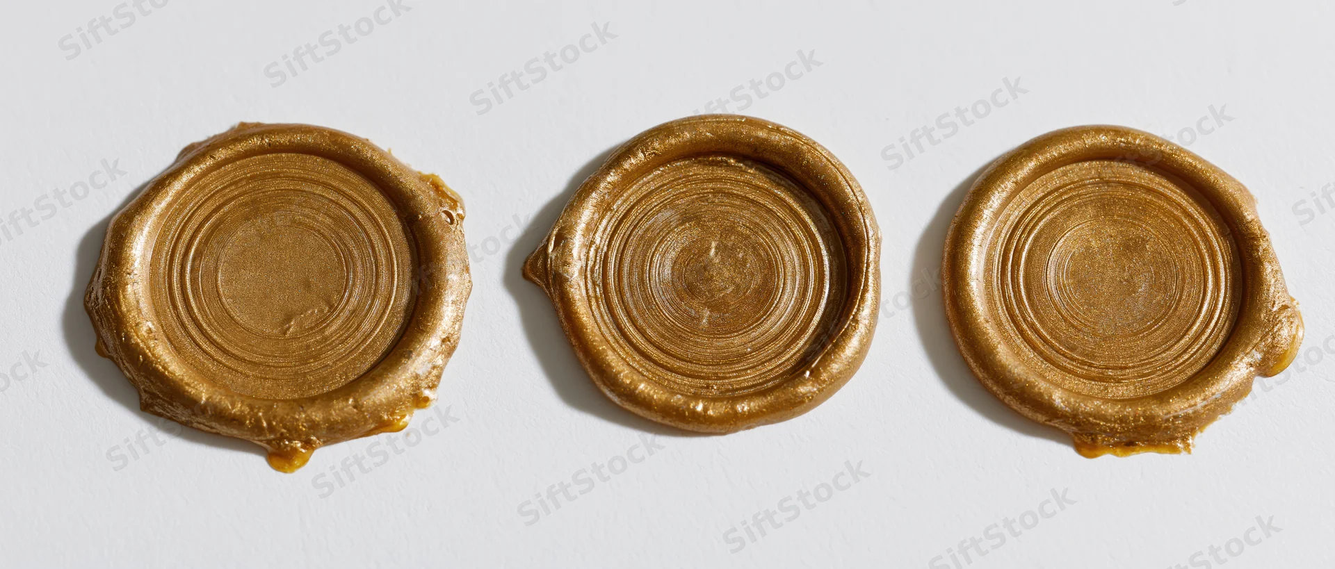 Three blank gold wax seals arranged in a horizontal row on a white surface