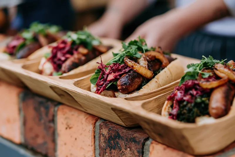 Gourmet hot dogs with toppings served in wooden boat trays on a brick surface