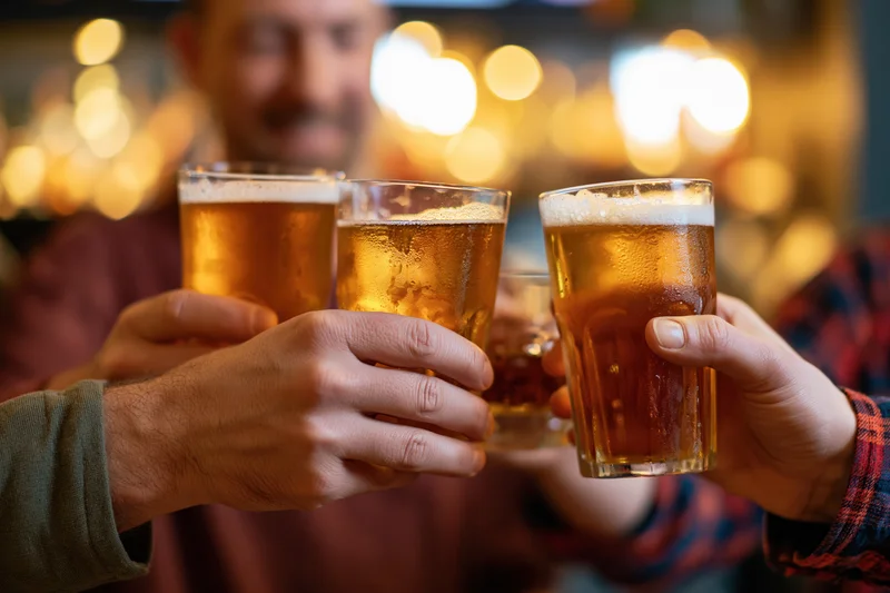 Three hands clinking amber beer glasses in a warm-lit pub