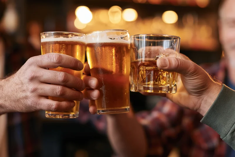 Three hands clinking glasses of amber beer and whiskey in a bar