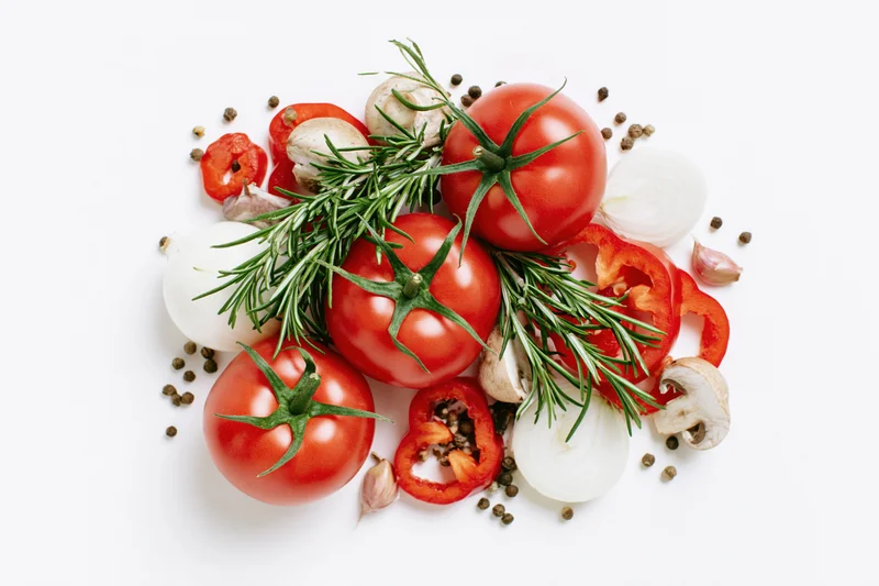 Ripe tomatoes with rosemary, onions, garlic, mushrooms and peppers arranged on white background