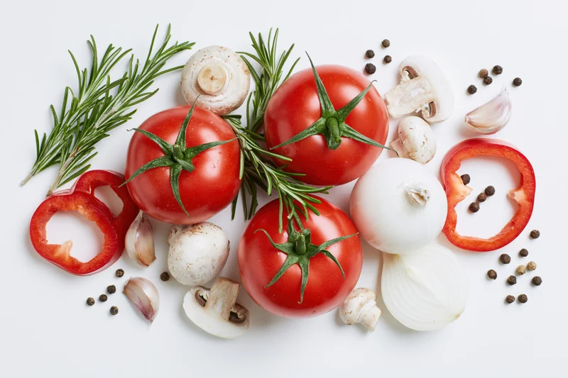 Ripe tomatoes with fresh herbs, vegetables and spices arranged on white surface