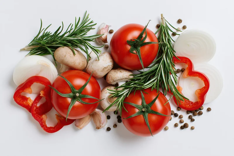 Ripe tomatoes with rosemary, garlic, onions, peppers and mushrooms arranged on white background
