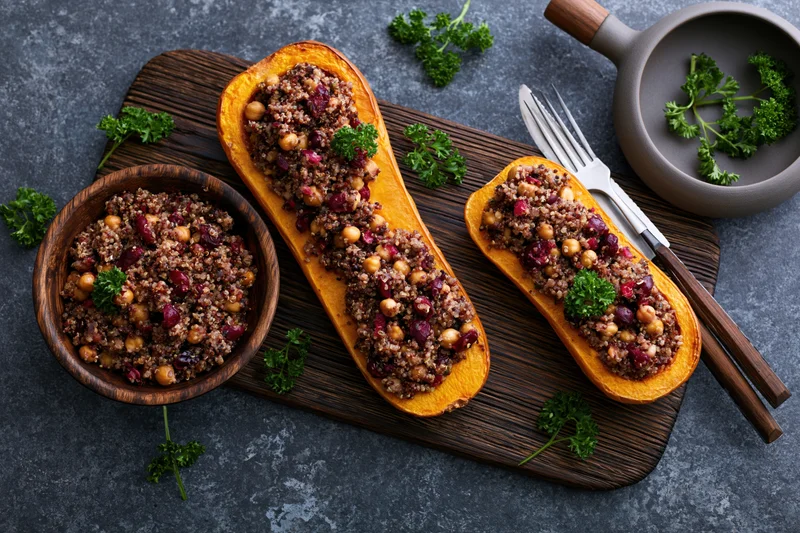 Roasted butternut squash halves stuffed with quinoa and chickpeas on a wooden board with parsley garnish