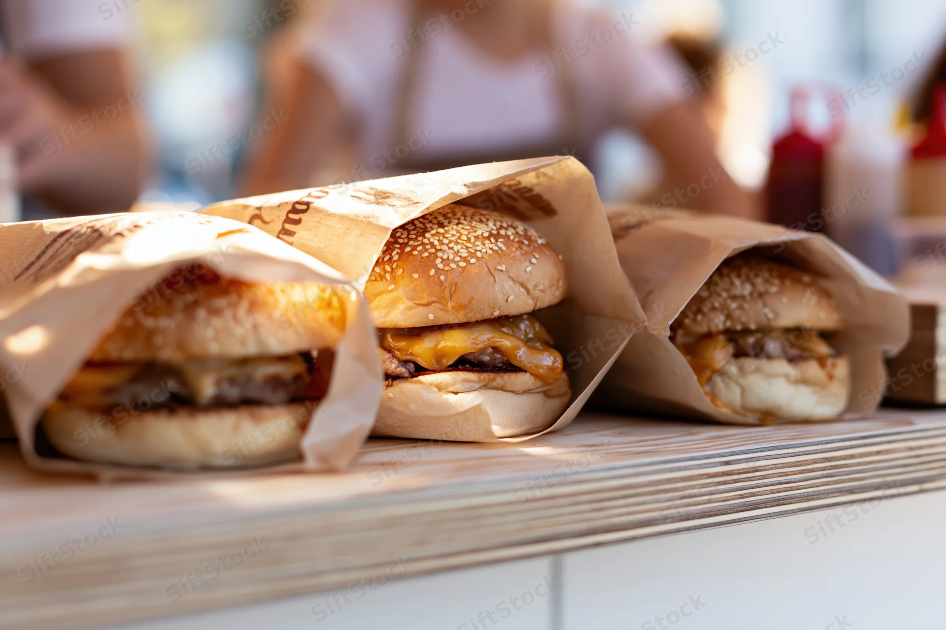Three cheeseburgers wrapped in branded parchment paper on a wooden counter