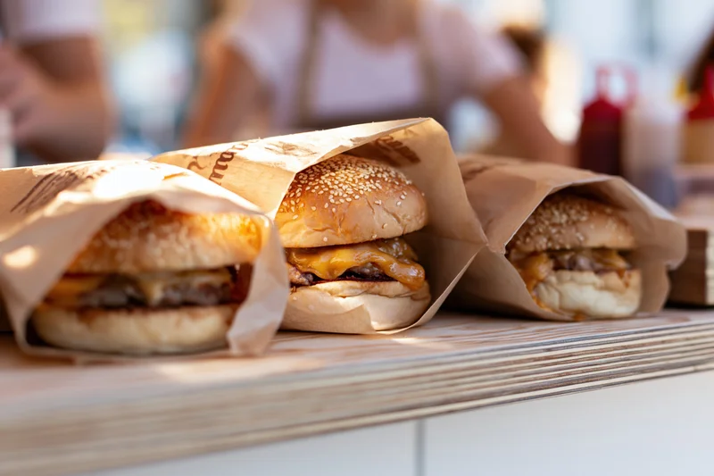 Three cheeseburgers wrapped in branded parchment paper on a wooden counter