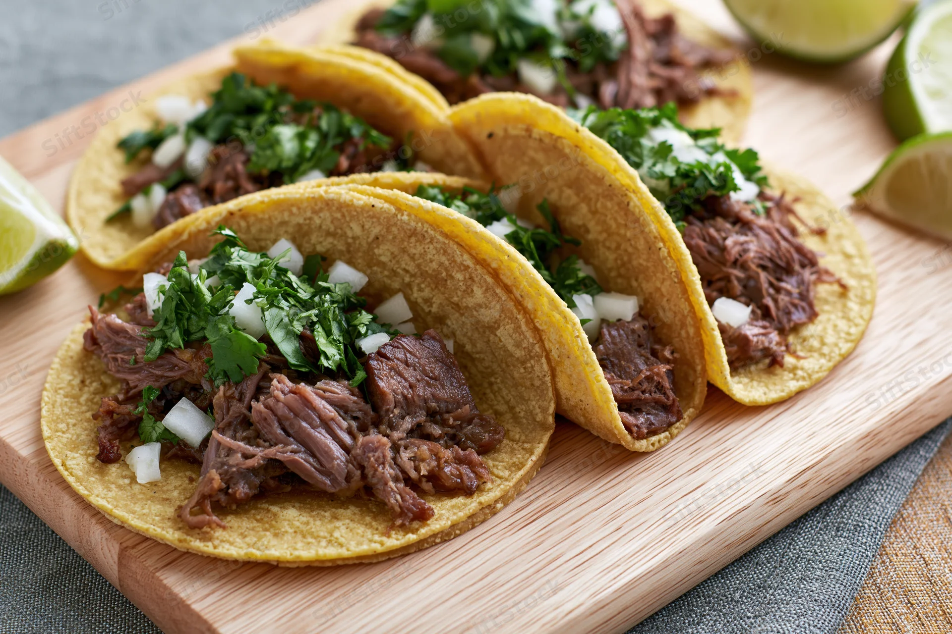 Four beef tacos with cilantro and onion on a wooden cutting board
