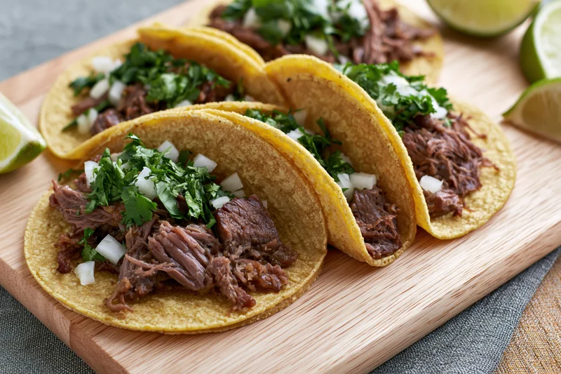 Four beef tacos with cilantro and onion on a wooden cutting board