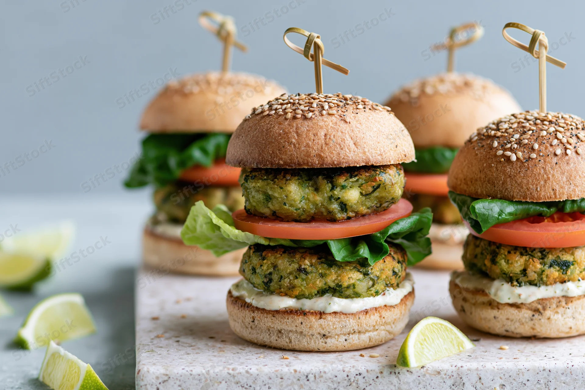 Stacked veggie burgers with sesame buns and lime garnish on stone platter