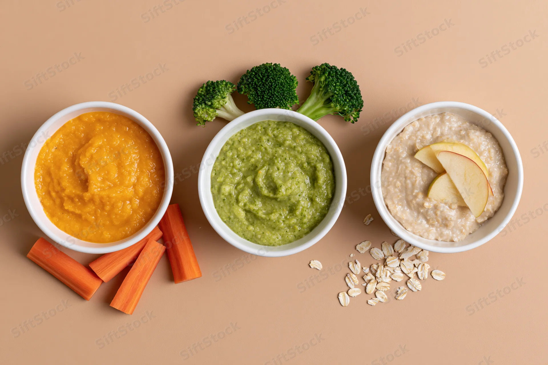 Three white bowls of baby food puree with vegetables and oats arranged on a beige surface